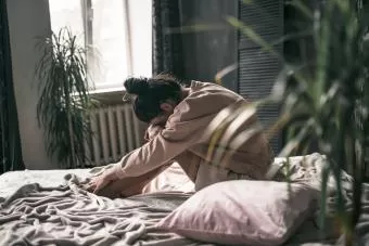 A young woman sits alone on her bed, appearing sad and lost in thought, symbolizing grief after loss.
