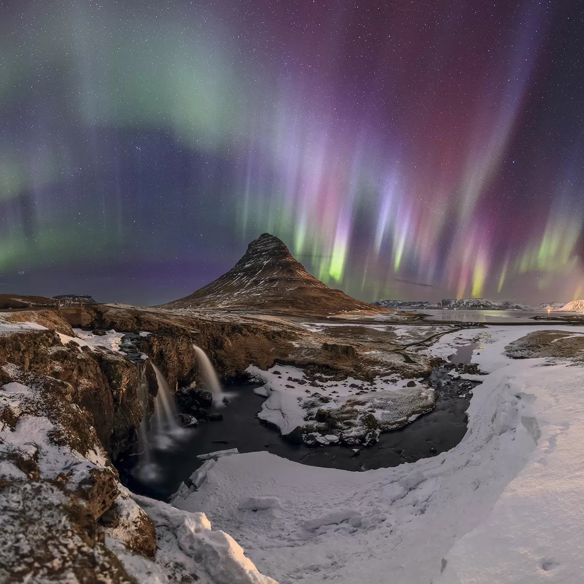 Vibrant northern lights over a dark landscape in Iceland with visible stars.